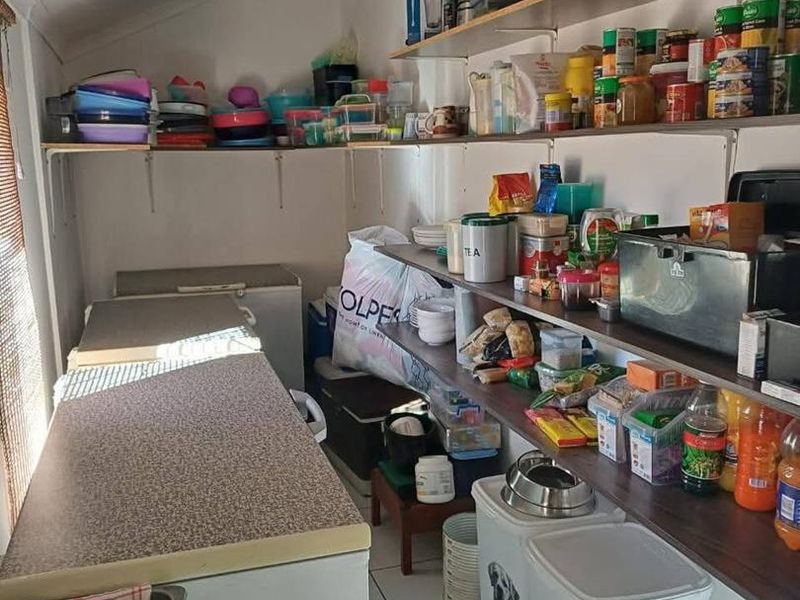 A functional scullery or pantry area featuring extensive wall-mounted shelving and laminate countertop workspace, providing ample storage for kitchen essentials.