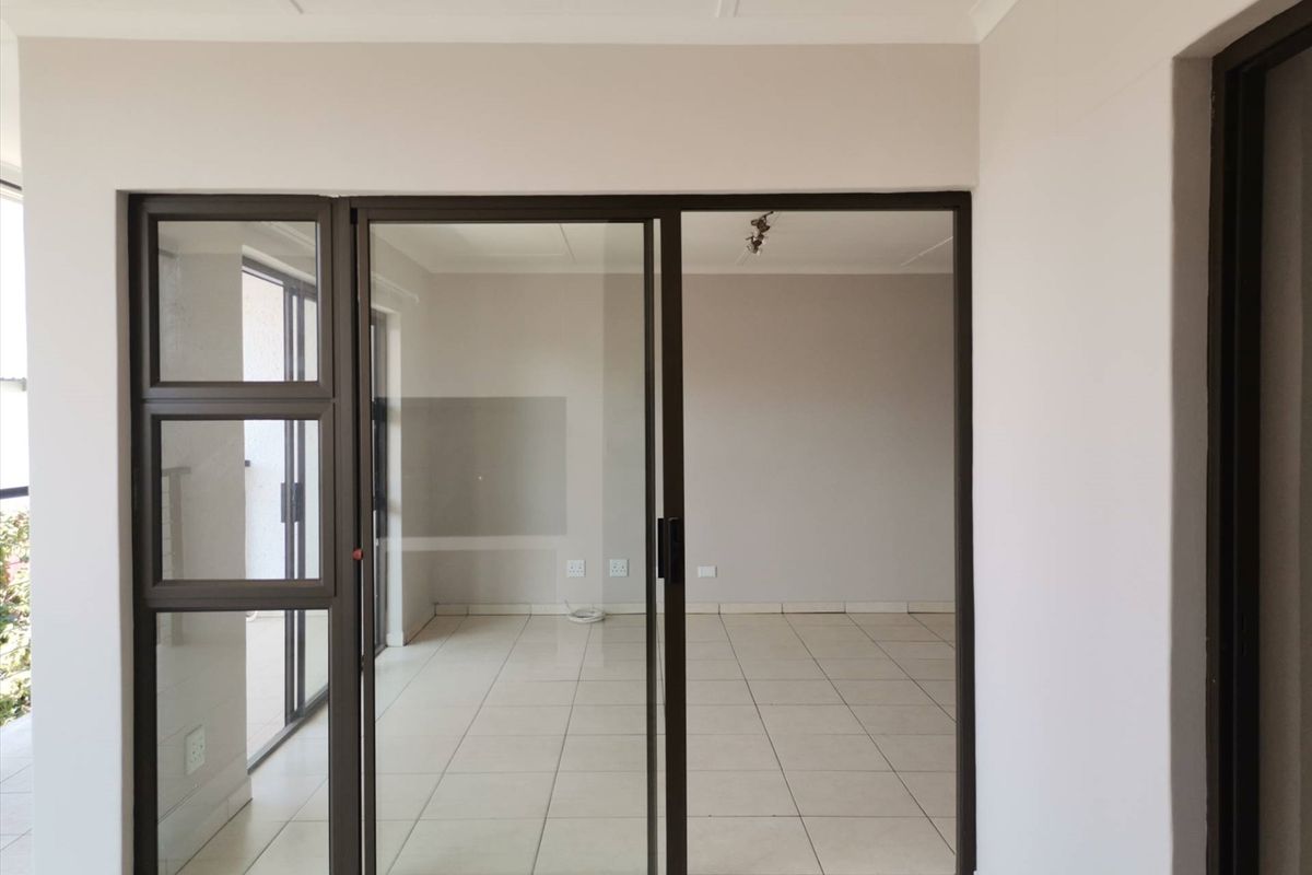 An empty, well-lit living area featuring neutral tiled flooring and modern aluminium sliding glass doors leading to an adjacent space.