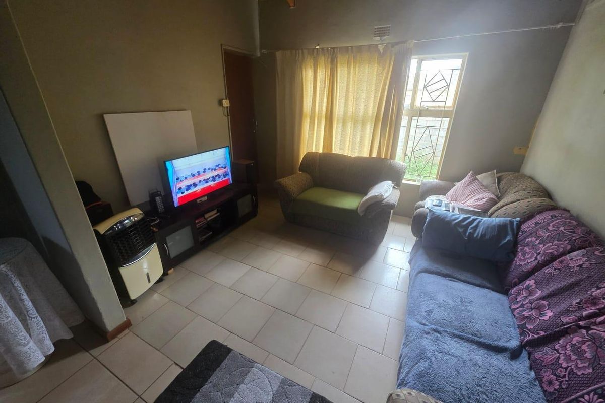A living room featuring tiled flooring, exposed timber ceiling beams, and a window with security bars.