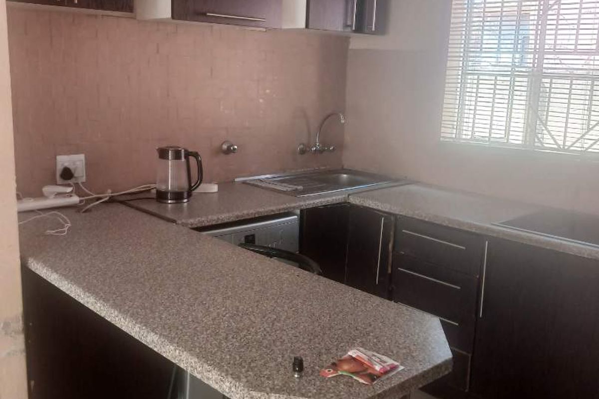 A functional kitchen featuring dark cabinetry, a breakfast bar with stone-look laminate countertop, stainless steel sink, and tiled flooring.