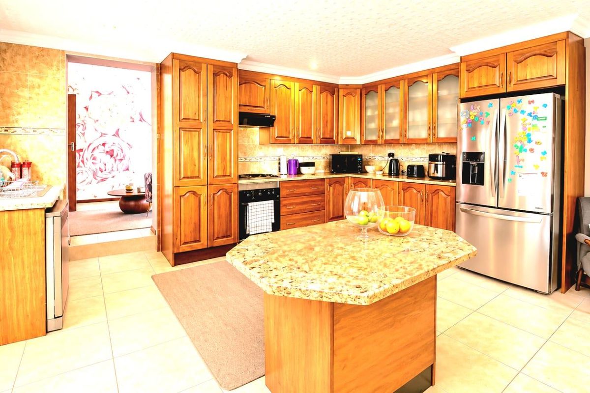 A functional kitchen featuring warm-toned wooden cabinetry, granite countertops, a central island, and tiled flooring, offering ample storage and workspace.