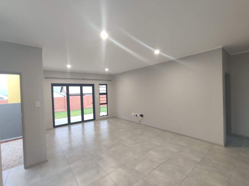 A bright, modern, and empty living room featuring neutral tiled flooring, recessed downlighting, and large aluminium sliding doors providing access to the outdoor area.