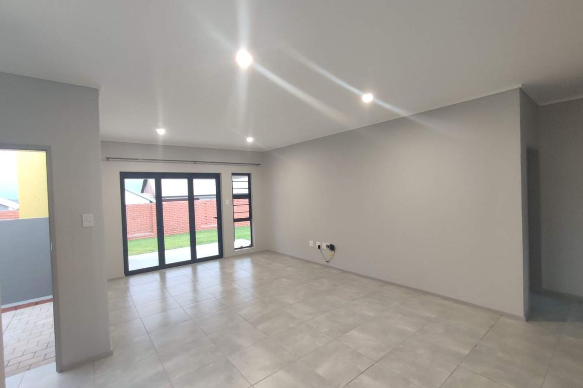 A bright, modern, and empty living room featuring neutral tiled flooring, recessed downlighting, and large aluminium sliding doors providing access to the outdoor area.
