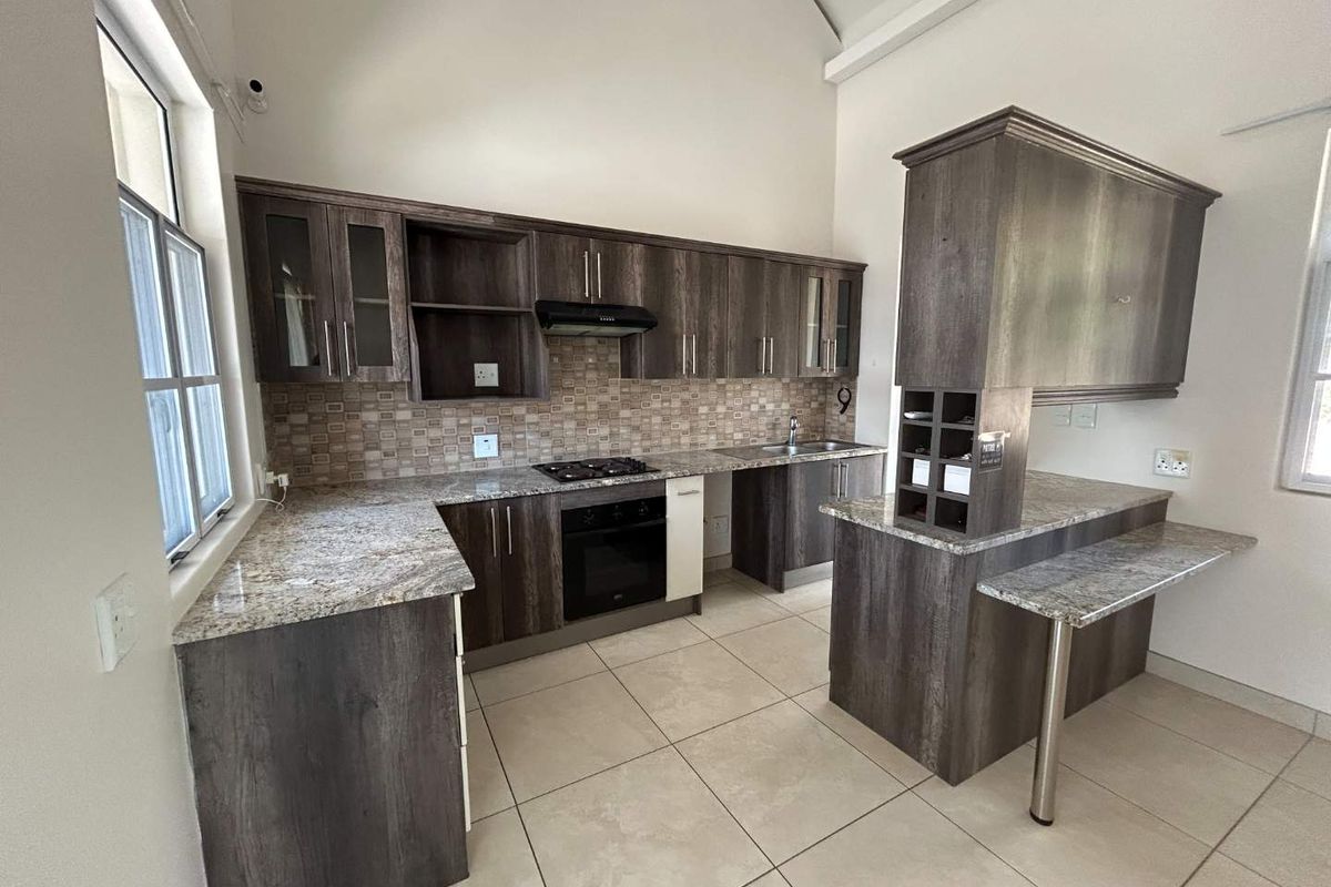 Modern kitchen featuring dark wood cabinetry, granite countertops, built-in oven, gas hob, and a breakfast bar, set under a high vaulted ceiling.
