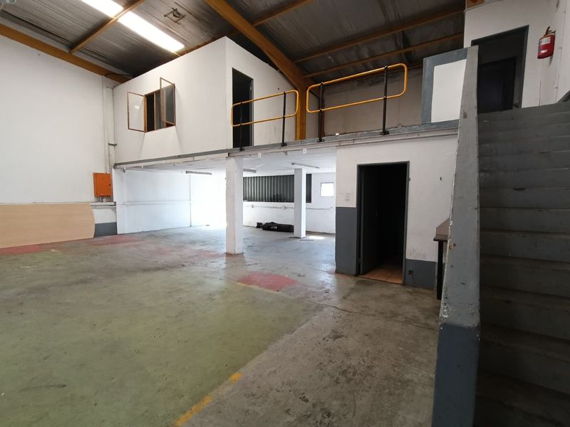 Spacious industrial warehouse unit featuring a mezzanine level, concrete flooring, steel staircase, and exposed roof trusses, suitable for various commercial or storage applications.