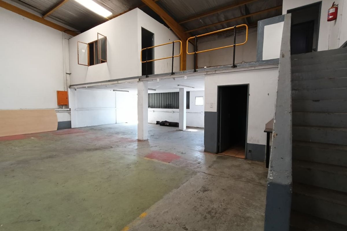 Spacious industrial warehouse unit featuring a mezzanine level, concrete flooring, steel staircase, and exposed roof trusses, suitable for various commercial or storage applications.