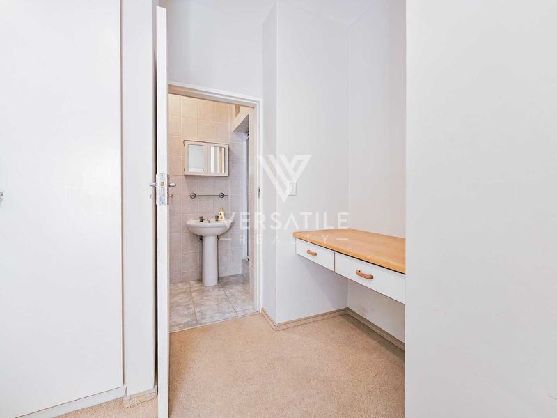 A functional bathroom area featuring a pedestal basin and an adjacent built-in vanity desk with storage drawers.