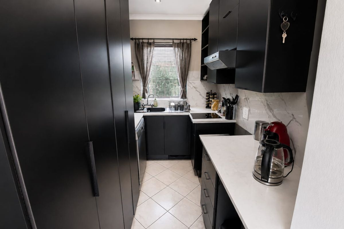 Modern galley-style kitchen featuring sleek black cabinetry, stone countertops, marble-look splashbacks, and integrated appliances in a well-maintained space.