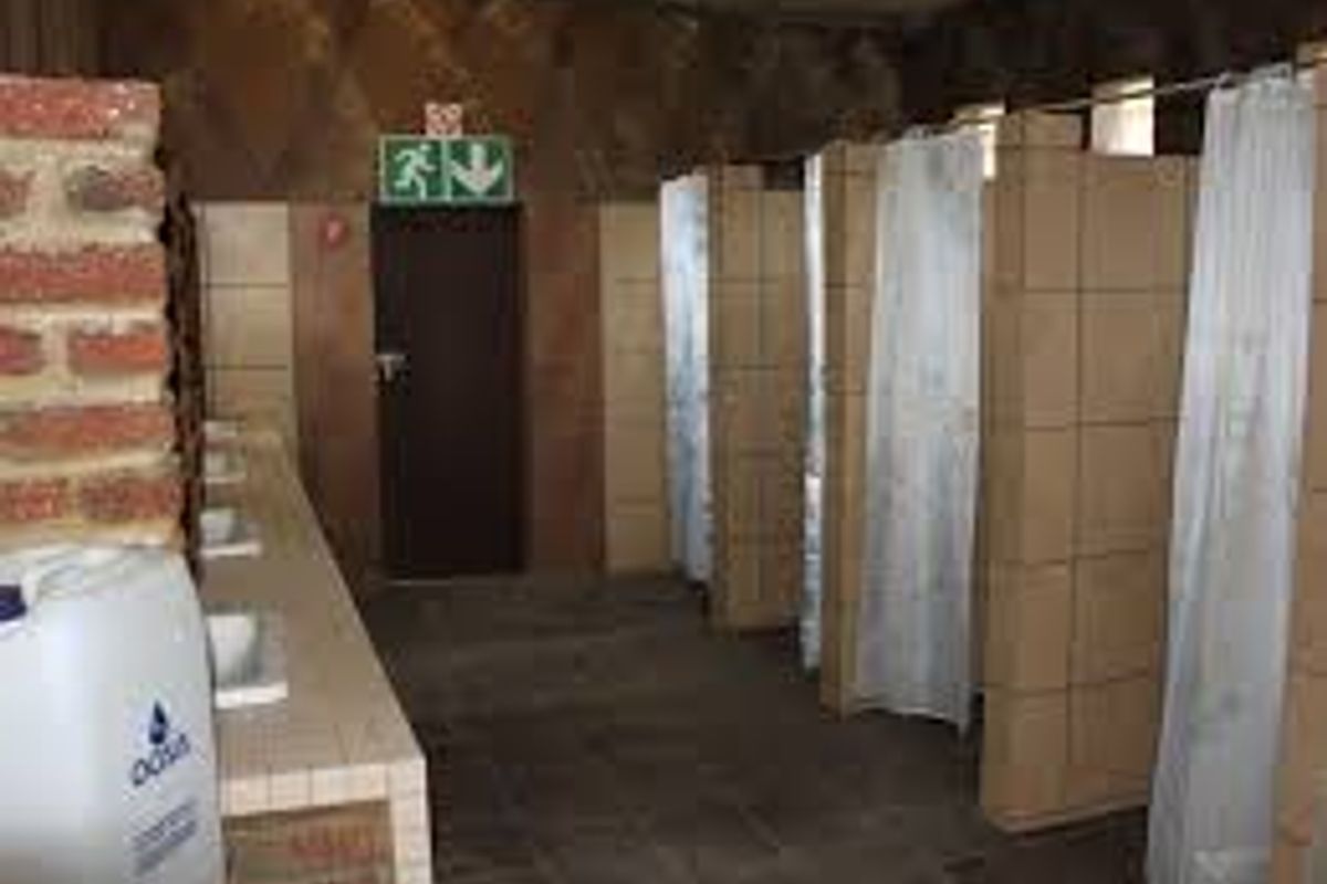 Communal bathroom facility featuring multiple tiled shower cubicles, a long vanity counter with integrated basins, and industrial-style finishes.