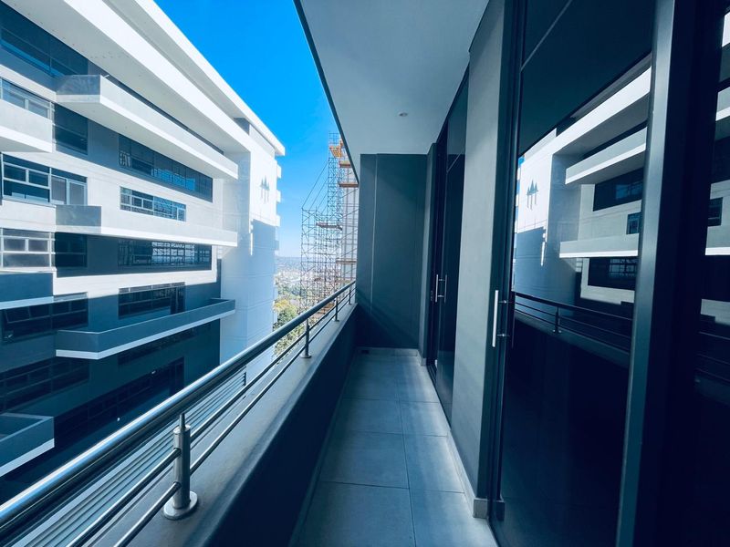 A modern, covered balcony featuring tiled flooring and a stainless steel balustrade, offering views of the surrounding apartment complex.