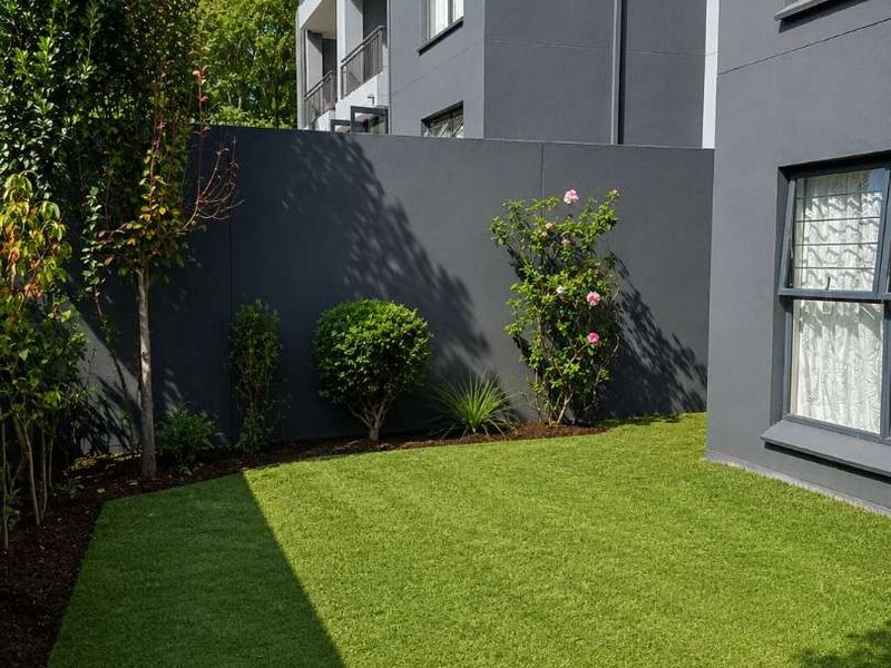 A well-maintained private rear garden area featuring artificial turf, landscaped garden beds, and a modern boundary wall adjacent to the apartment building.