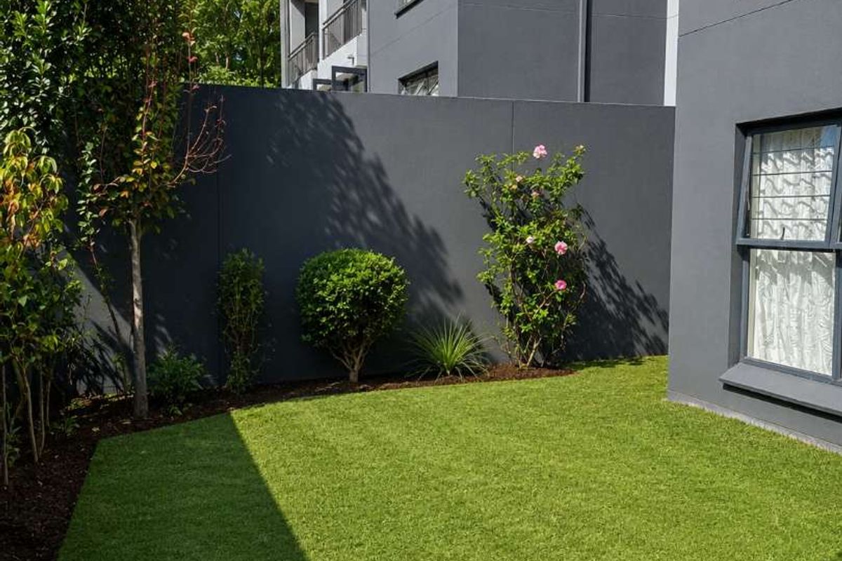 A well-maintained private rear garden area featuring artificial turf, landscaped garden beds, and a modern boundary wall adjacent to the apartment building.