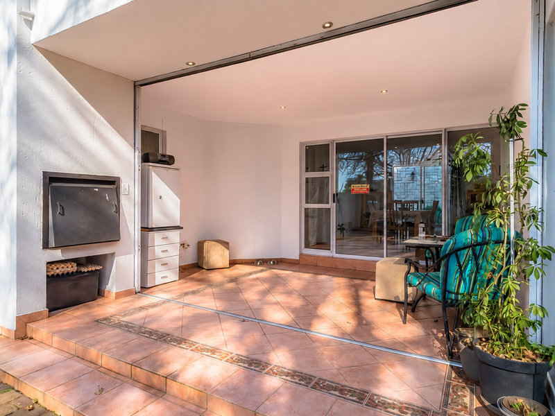 Covered patio area featuring tiled flooring, recessed downlights, and a built-in braai, seamlessly connecting to the interior living space through large sliding glass doors.
