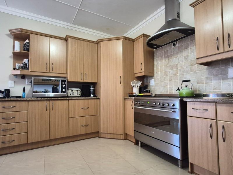 A functional kitchen featuring light wood-tone cabinetry, a stainless steel freestanding oven with extractor fan, tiled backsplash, and neutral floor tiles.