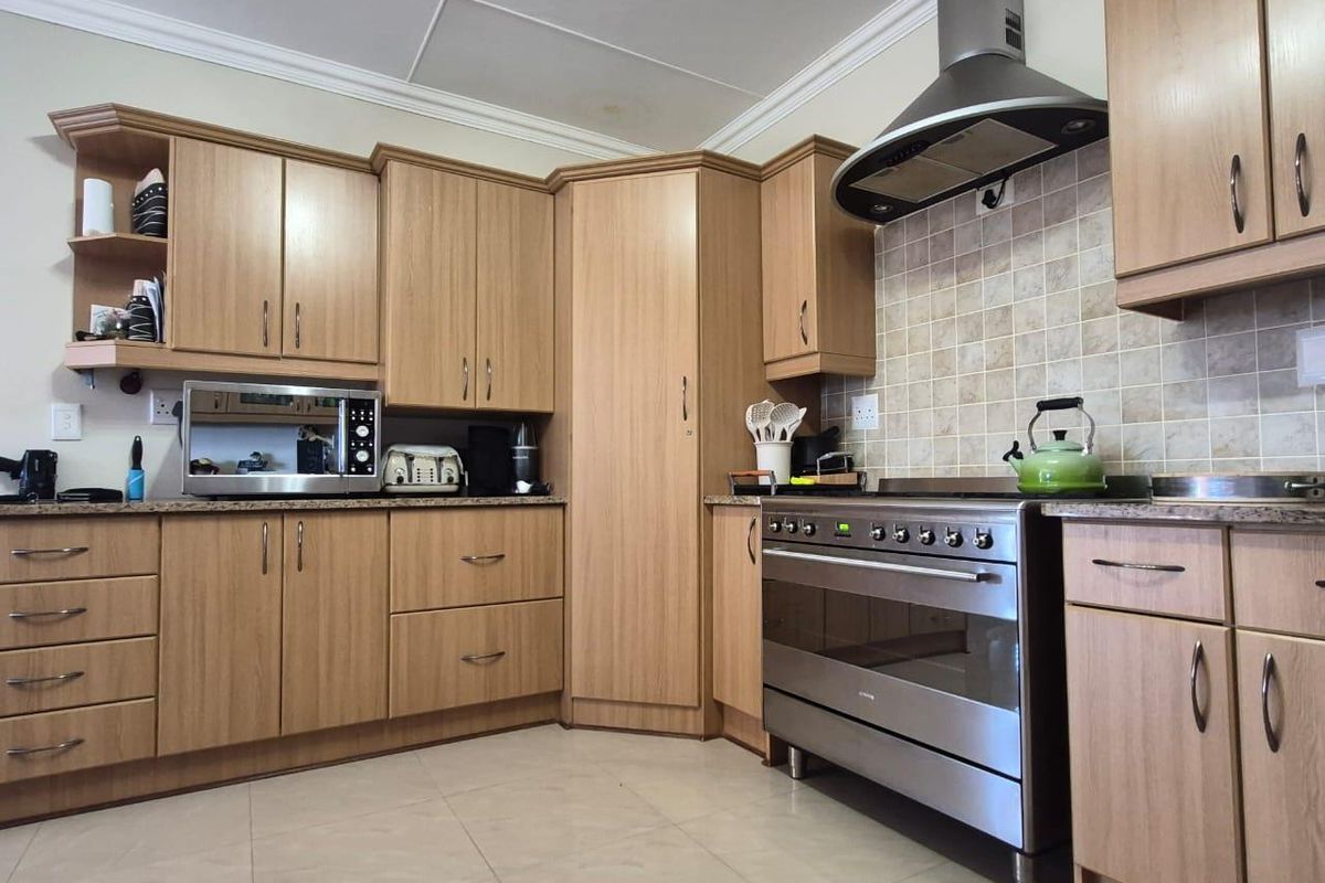 A functional kitchen featuring light wood-tone cabinetry, a stainless steel freestanding oven with extractor fan, tiled backsplash, and neutral floor tiles.