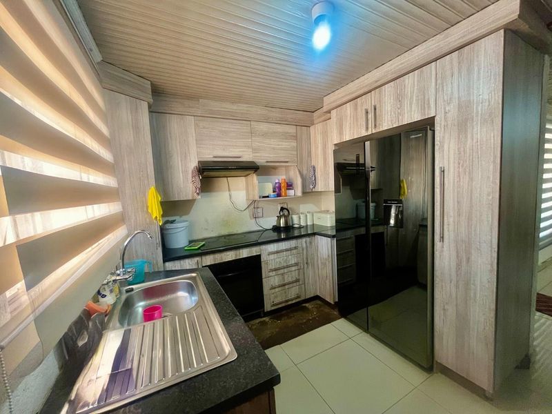 Compact kitchen featuring wood-look cabinetry, stainless steel sink, built-in oven, and extractor fan, with tiled flooring and panelled ceiling.
