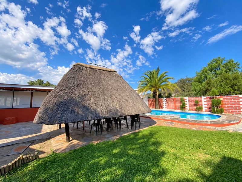 Outdoor entertainment area featuring a traditional thatched lapa, swimming pool, stone-paved patio, and landscaped garden with a brick boundary wall.