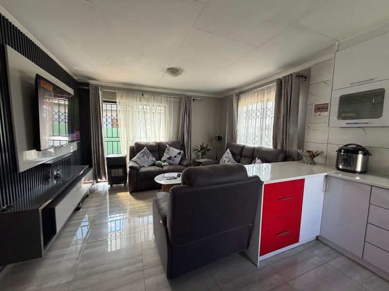 An open-plan living and kitchen area featuring modern tiled flooring, a built-in media wall, and a kitchen island with contrasting cabinetry.