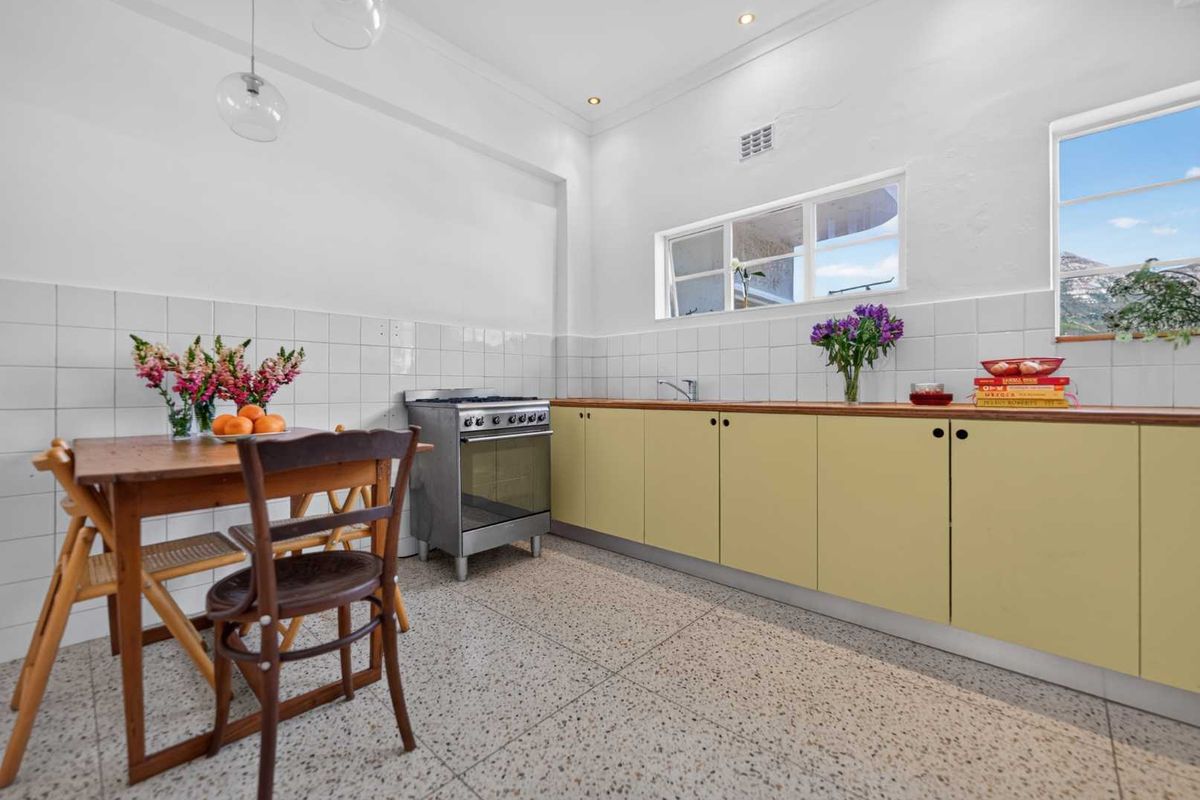 A functional kitchen featuring terrazzo flooring, light-toned cabinetry, a freestanding oven, and a tiled splashback with ample natural light.