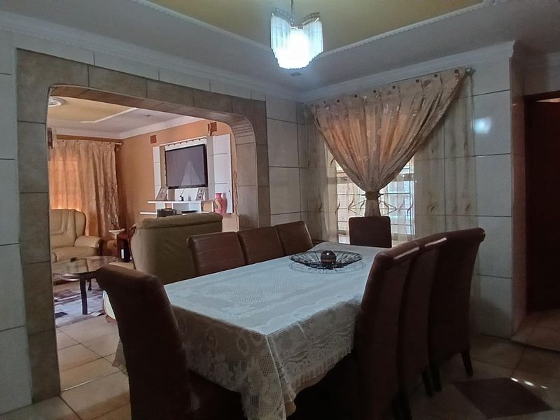 Open plan dining and living area featuring tiled flooring, a decorative archway, and coved ceiling details, creating a connected and functional living space.