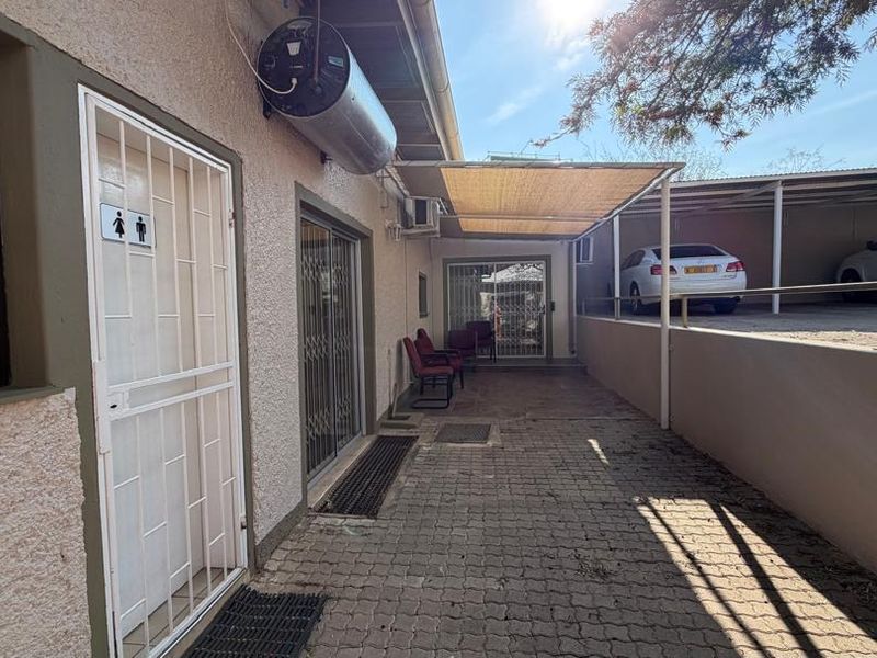 Rear exterior view of the office building featuring a paved walkway, security gates, sliding doors, and an adjacent covered carport area.
