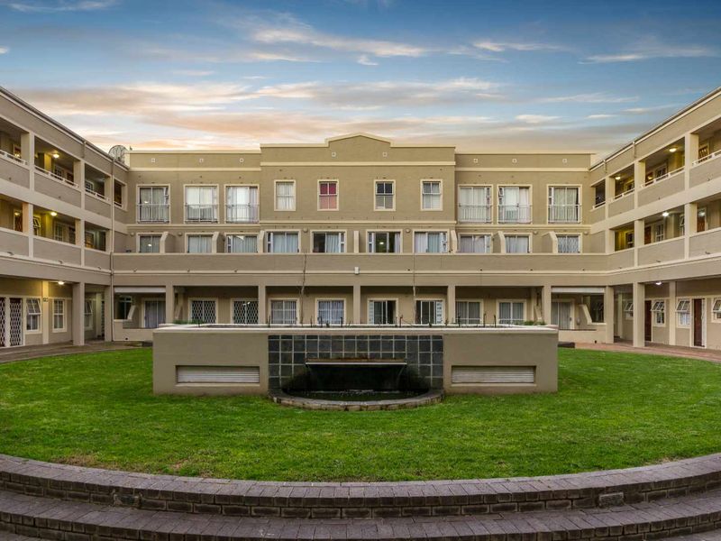A well-maintained apartment complex courtyard featuring a central water feature, manicured lawn, and multi-level residential units with private balconies.