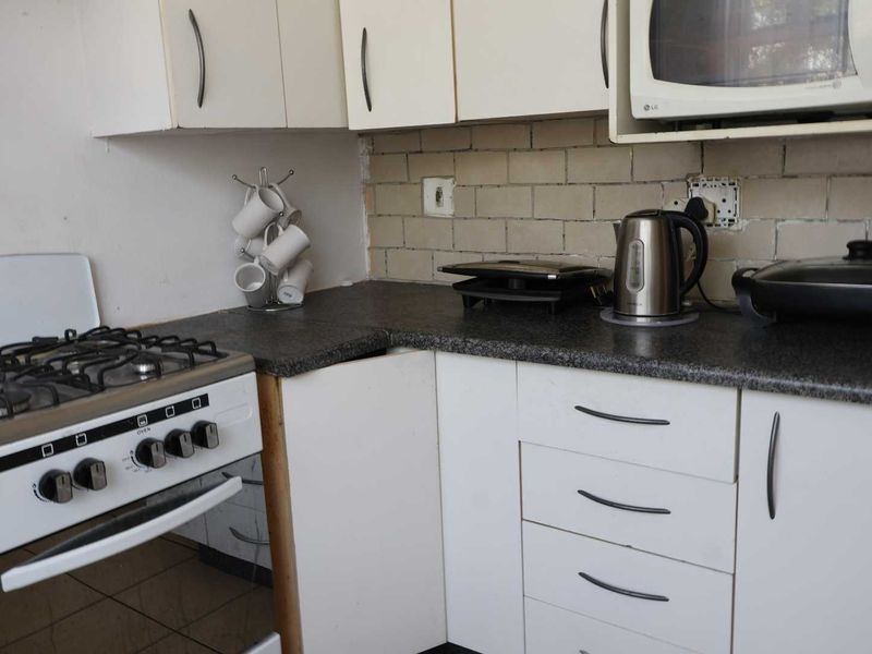 A compact kitchen featuring white cabinetry, a gas stove, built-in microwave, and tiled backsplash, currently showing signs of wear and requiring maintenance.