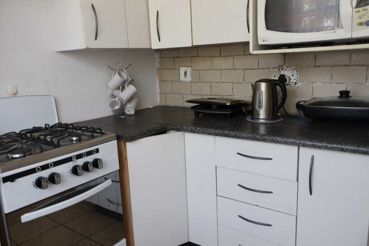 A compact kitchen featuring white cabinetry, a gas stove, built-in microwave, and tiled backsplash, currently showing signs of wear and requiring maintenance.