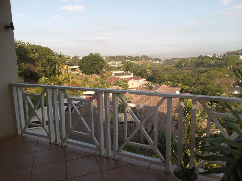 A balcony featuring tiled flooring and a wooden balustrade, offering elevated views of the surrounding residential area and lush greenery.