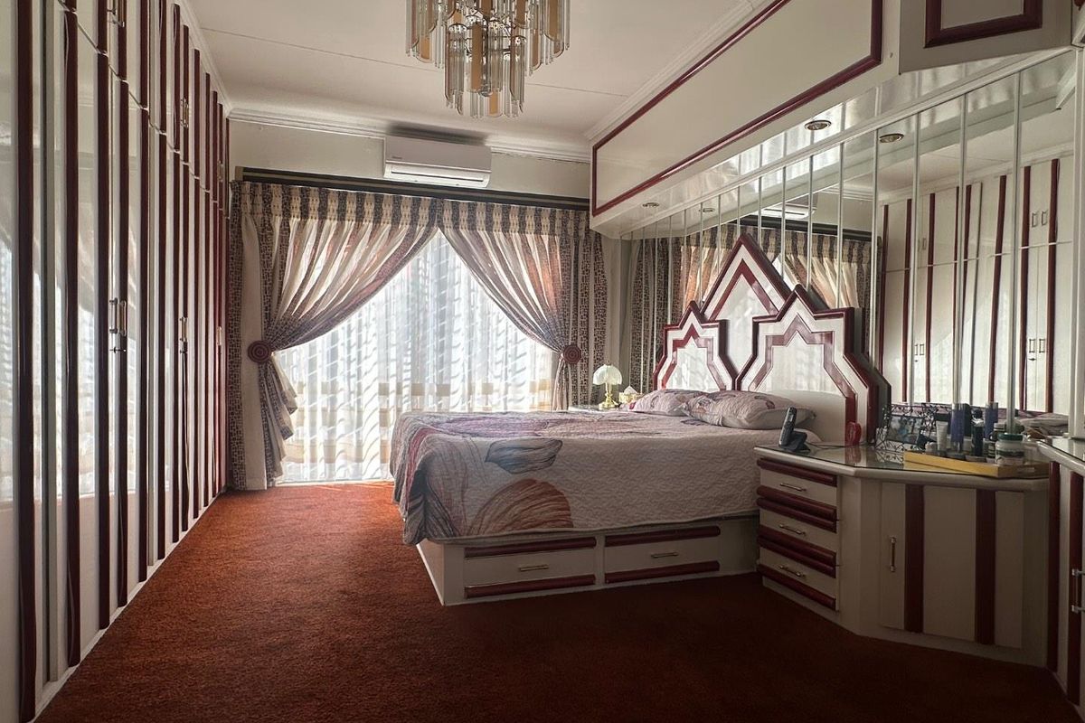 Spacious bedroom featuring extensive built-in cabinetry, mirrored wall panels, integrated headboard, and a wall-mounted air conditioning unit.