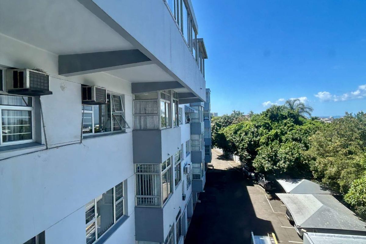 Exterior view of the apartment building facade showing window configurations, external air conditioning units, and the adjacent parking area.