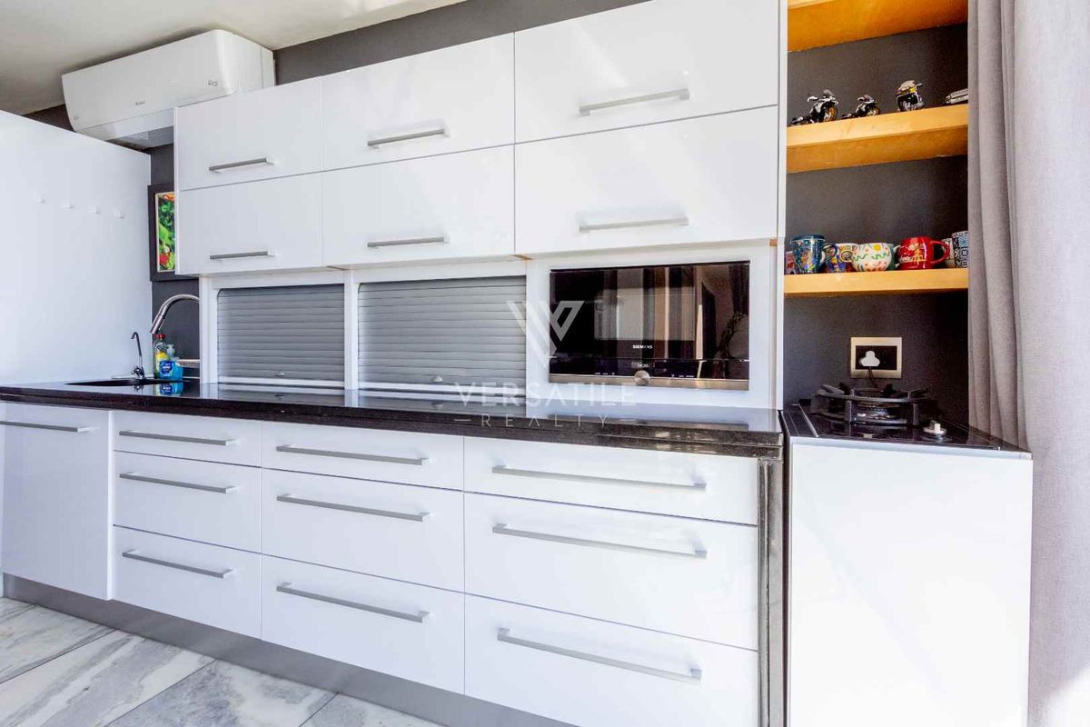 Modern kitchen featuring high-gloss white cabinetry, dark stone countertops, integrated microwave, and a gas hob, complemented by open shelving and a wall-mounted air conditioner.