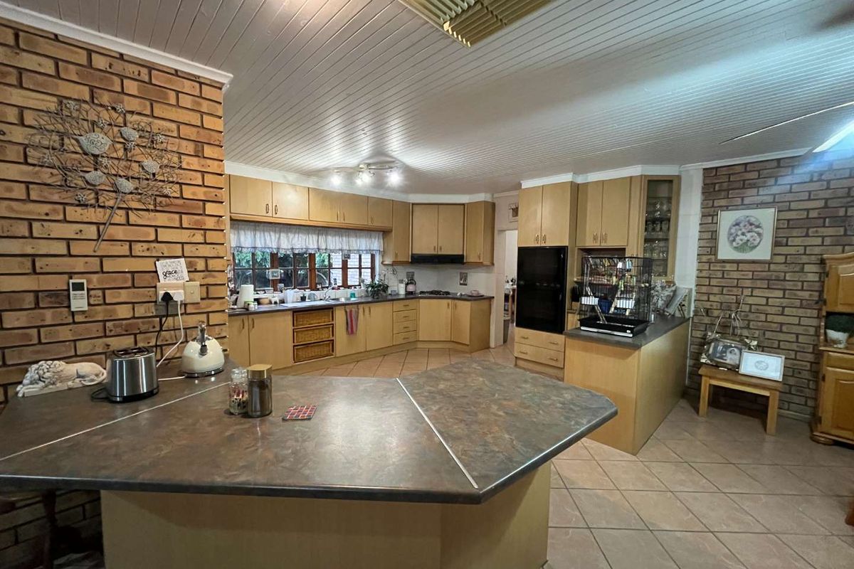 Spacious kitchen featuring extensive wooden cabinetry, built-in oven, integrated cooktop, and a large central breakfast bar with tiled flooring throughout.