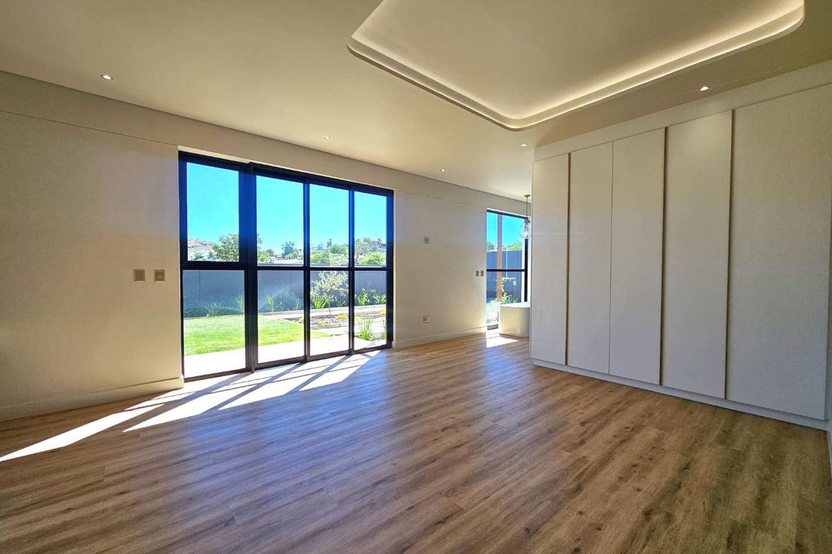 Spacious bedroom featuring modern wood-look flooring, recessed ceiling lighting, and large floor-to-ceiling windows with views of the garden.