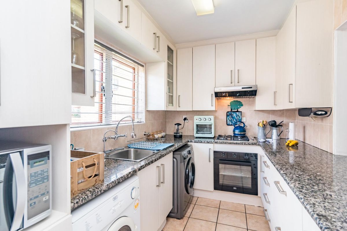 A functional kitchen featuring granite countertops, built-in cabinetry, a gas hob with extractor fan, and integrated space for laundry appliances.
