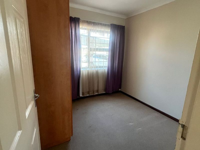 An empty bedroom featuring a built-in wardrobe, carpeted flooring, and a window with security bars.