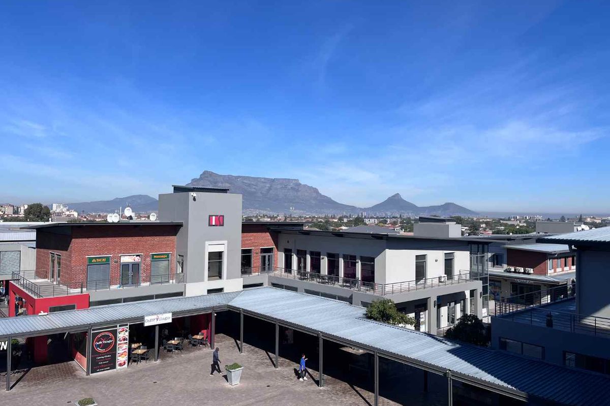 Elevated view of a modern office complex courtyard featuring covered walkways, brick and plaster facades, and a scenic mountain backdrop.