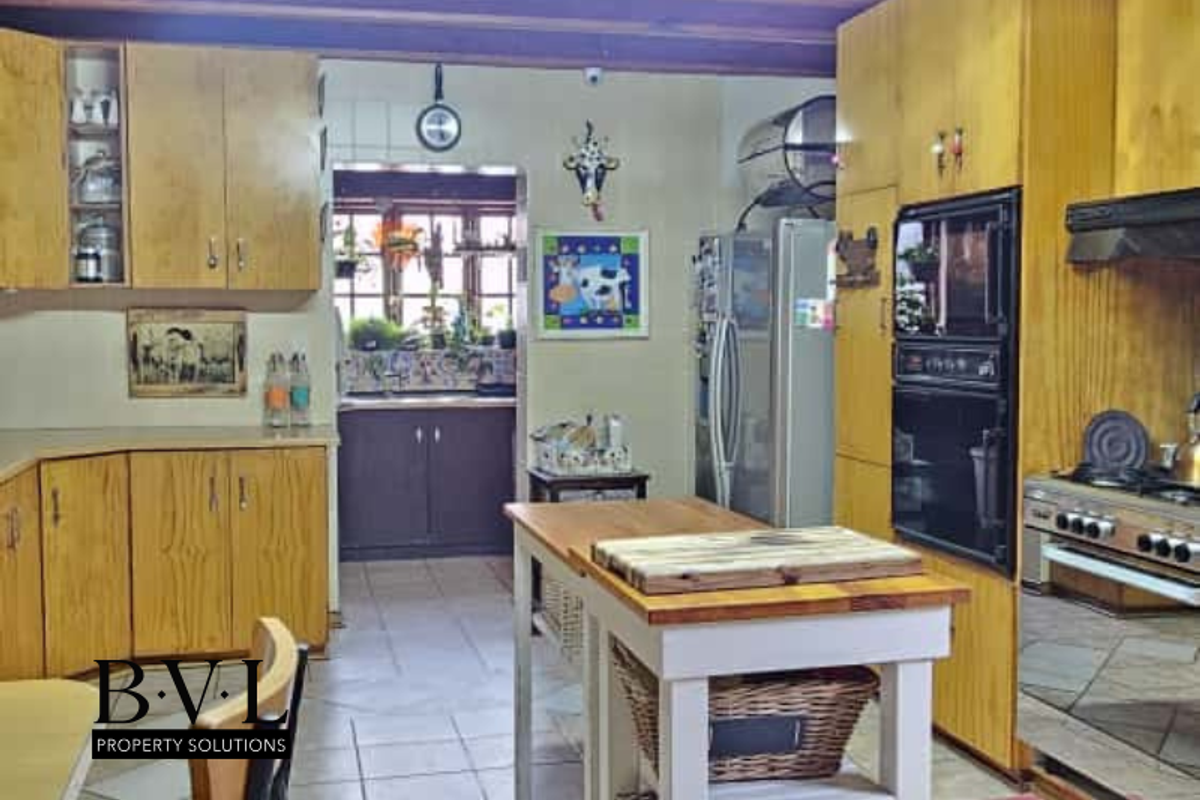A functional kitchen featuring timber cabinetry, built-in oven, gas hob, and a central island, with an adjoining scullery area visible in the background.