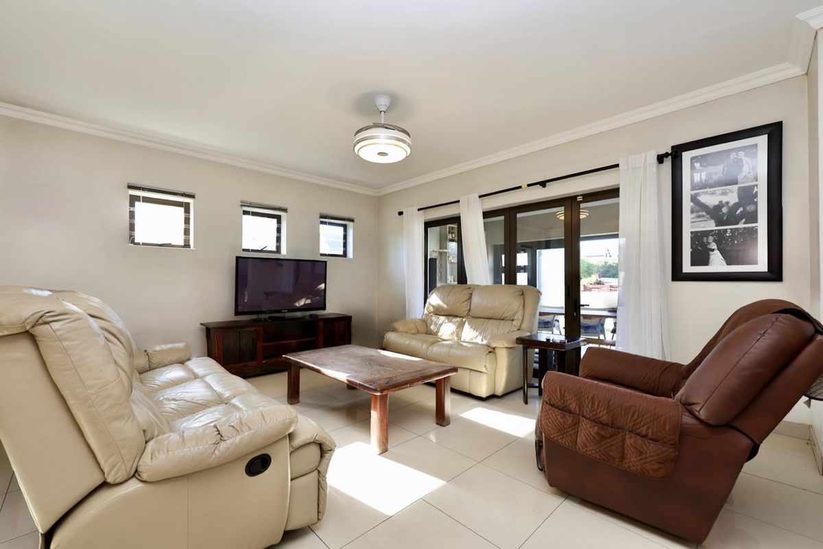 A bright and spacious living room featuring tiled flooring, a ceiling fan, and large sliding glass doors that open to an outdoor patio area.