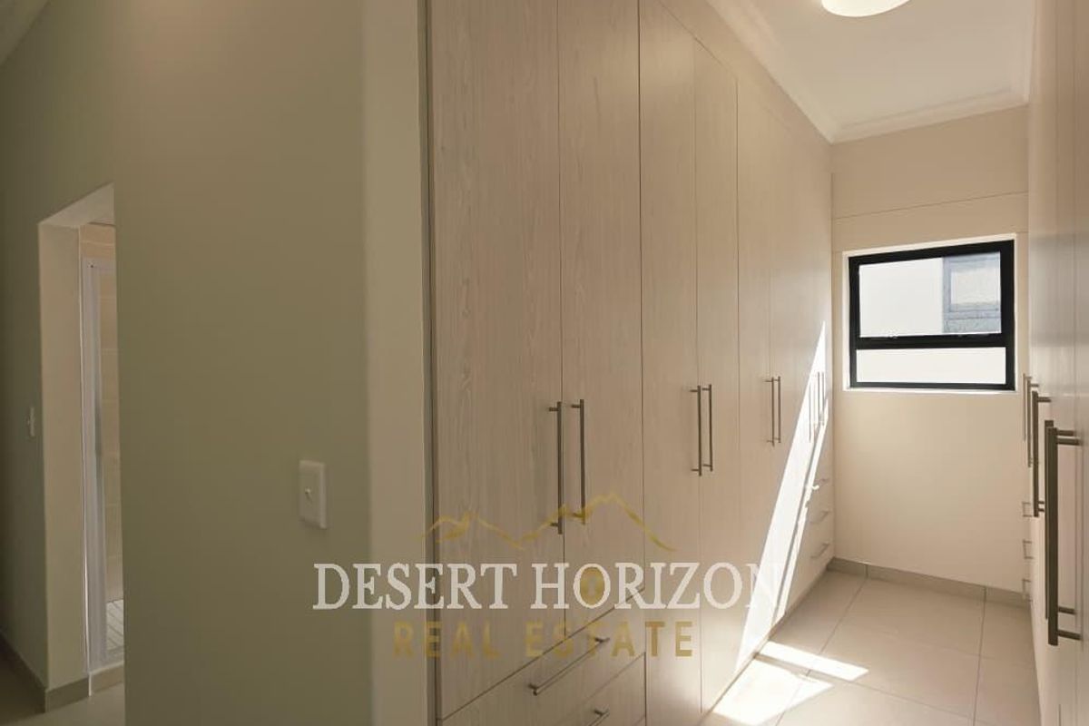 A modern walk-in closet featuring extensive built-in cabinetry with light wood-grain finish, tiled flooring, and a window for natural light.