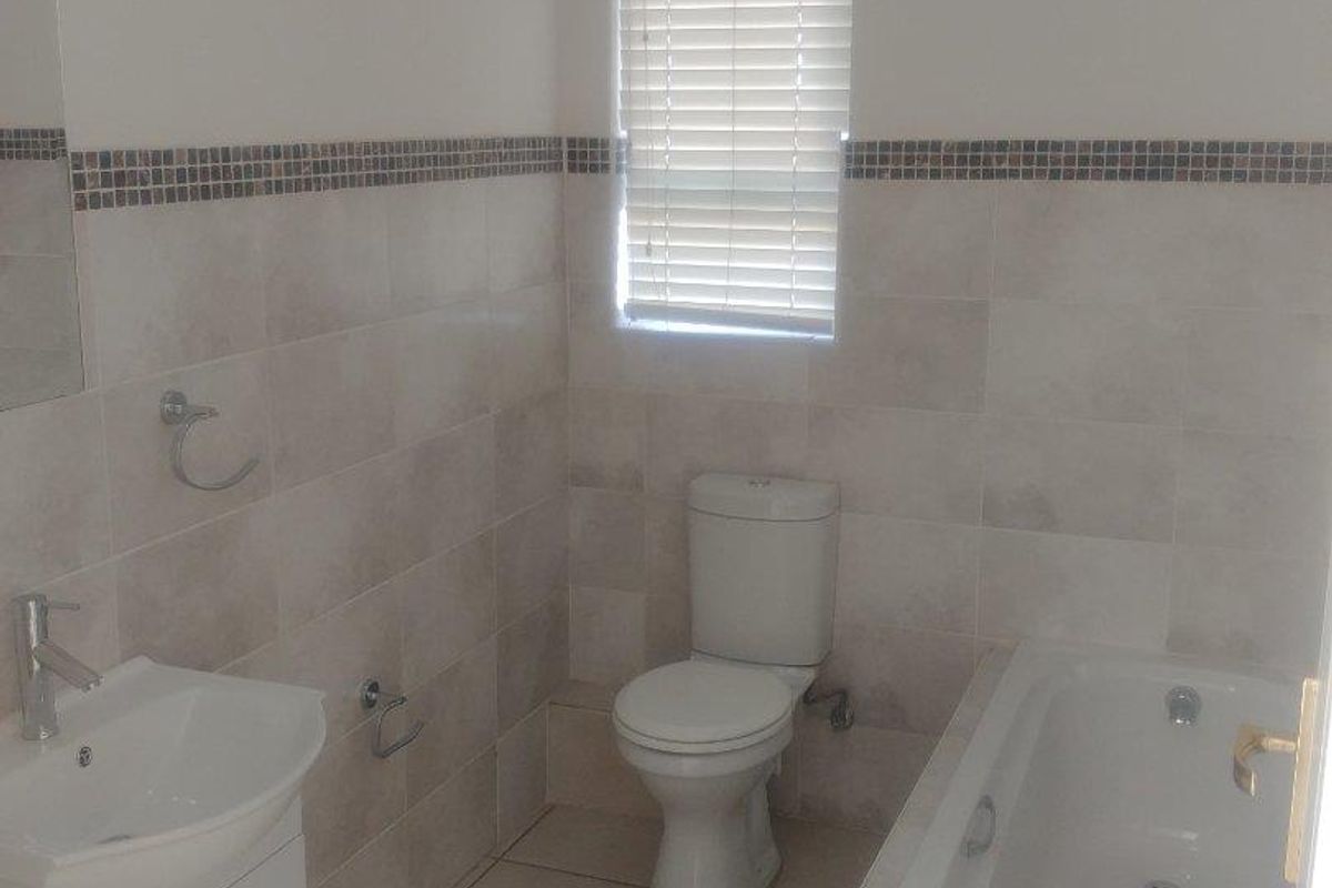 A functional bathroom featuring a white vanity basin, a standard bathtub, and a toilet, finished with neutral wall tiles and a decorative mosaic border.