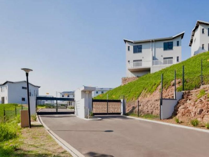 View of the secure gated entrance to the townhouse complex, featuring paved driveway, security gates, and perimeter electric fencing.