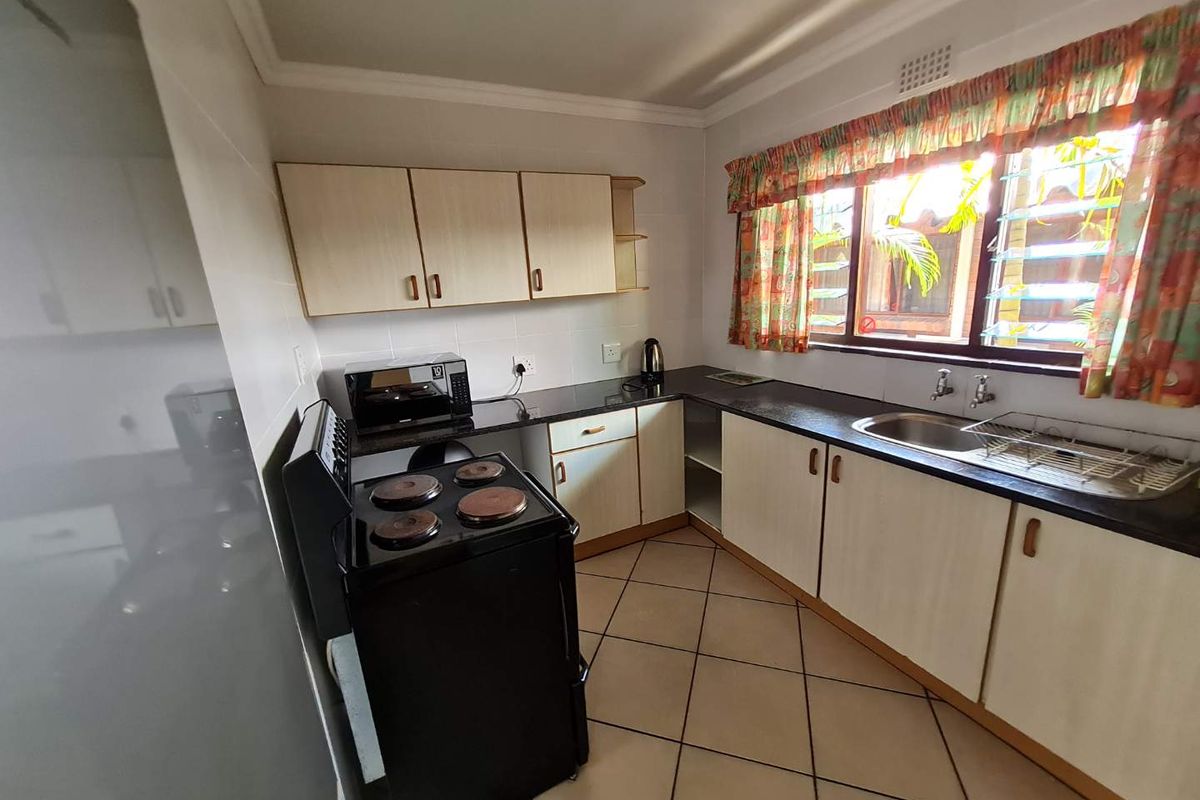 A functional kitchen featuring light-toned cabinetry, dark countertops, a stainless steel sink, and tiled flooring, offering a practical layout for daily meal preparation.