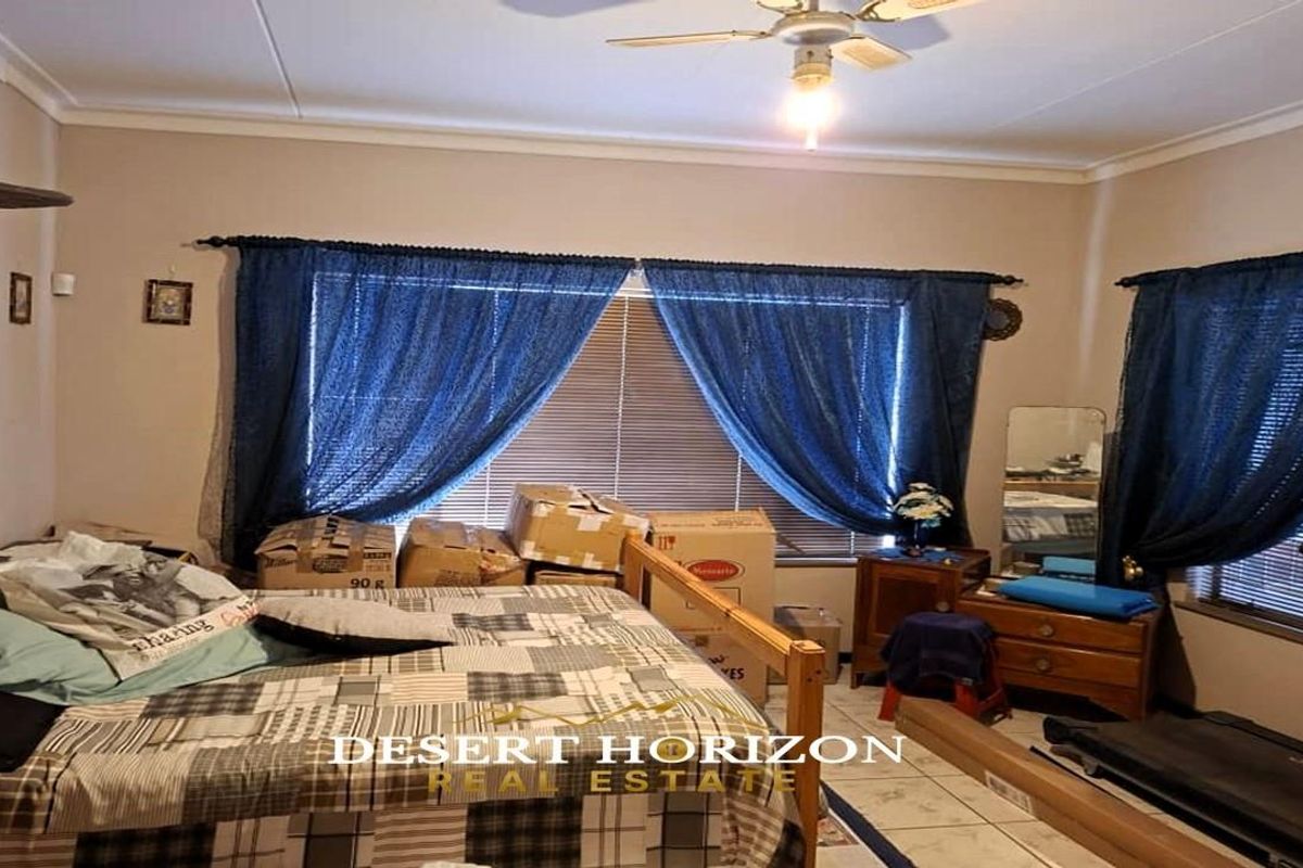 A bedroom featuring tiled flooring, a ceiling fan, and exposed brick wall detailing, providing a functional space with natural light through window blinds.