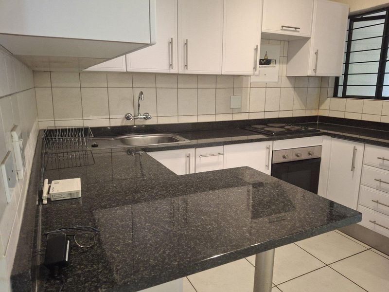 A functional kitchen featuring white cabinetry, dark granite countertops, a built-in oven, electric hob, and tiled backsplash with a window for natural light.