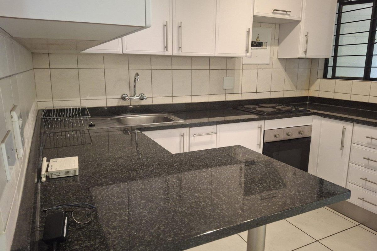 A functional kitchen featuring white cabinetry, dark granite countertops, a built-in oven, electric hob, and tiled backsplash with a window for natural light.
