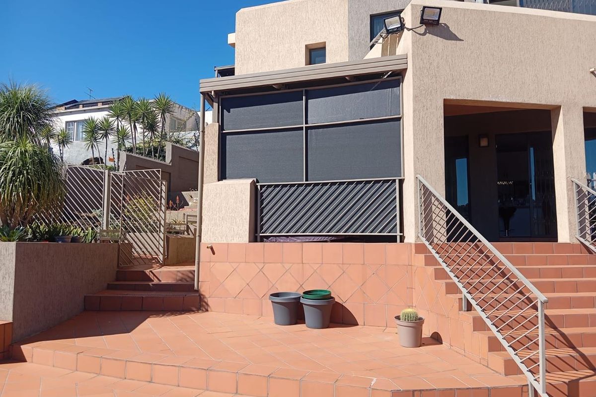 A rear patio area featuring terracotta-style tiled flooring, metal balustrades, and a covered section with privacy screening attached to the main building structure.