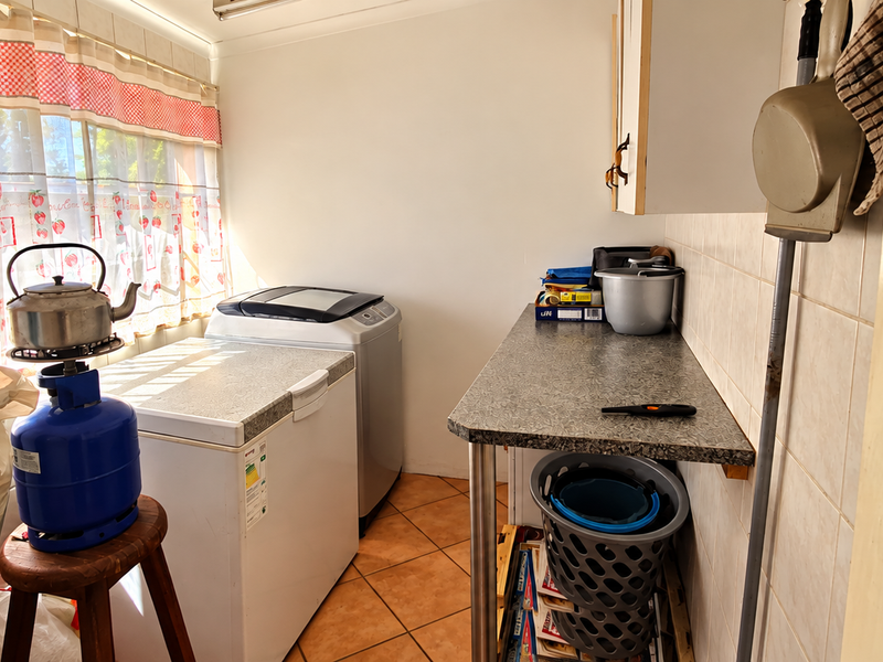 A functional laundry area featuring tiled flooring, wall tiling, and a laminate countertop with built-in cabinetry for storage and utility use.