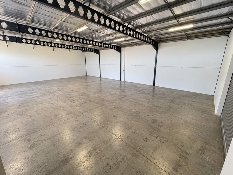 Spacious industrial warehouse unit featuring polished concrete floors, exposed steel roof trusses, and high-clearance ceilings, suitable for various commercial or storage applications.