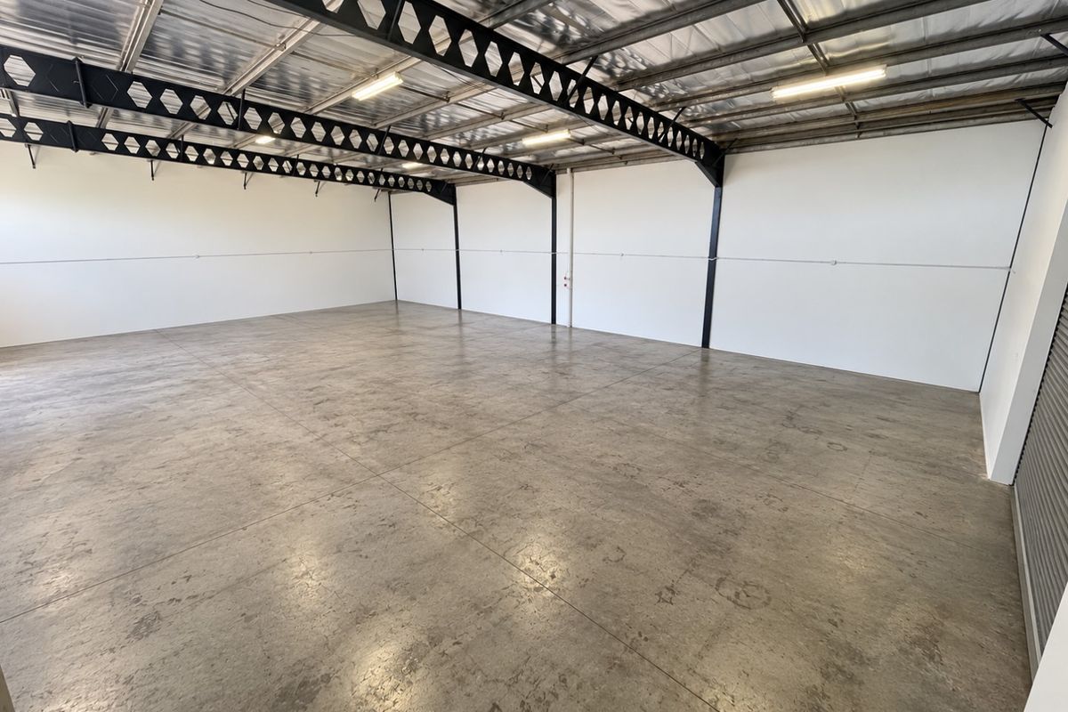 Spacious industrial warehouse unit featuring polished concrete floors, exposed steel roof trusses, and high-clearance ceilings, suitable for various commercial or storage applications.
